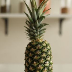 A vibrant pineapple stands in focus on a kitchen counter with spices in the background.